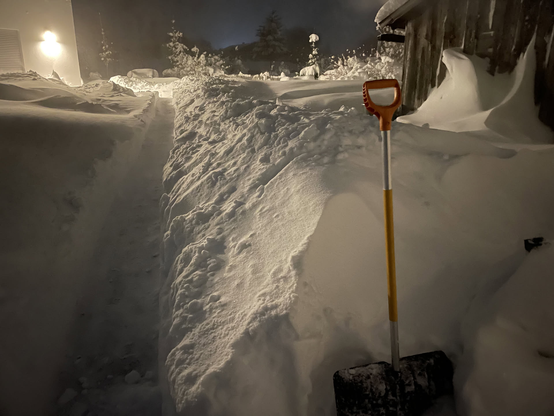 Nach dem Schneeräumen im Winter 2023. Ein schmaler geräumter Weg in der Dunkelheit. Rechts und links hohe Schneeberge vom intensiven Schaufeln.
